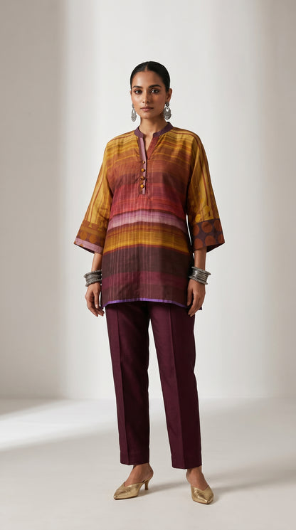 Woman wearing a patterned top and maroon pants on a plain background