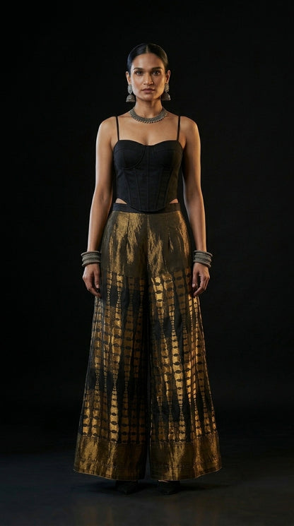 Woman wearing a black top and gold patterned plazzo against a black background