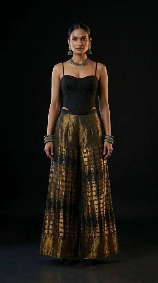 Woman wearing a black top and gold patterned plazzo against a black background