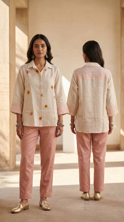 Woman wearing a beige shirt and pink pants standing in a sunlit room.