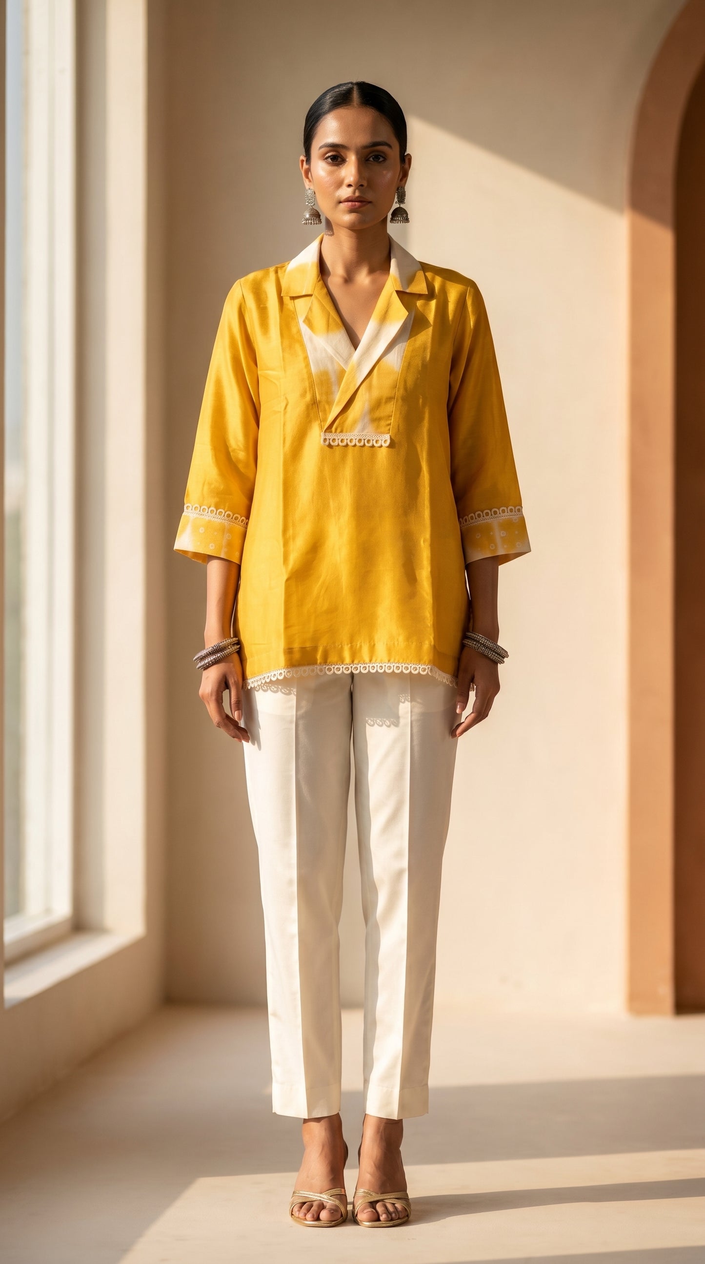 Woman wearing a yellow top and white pants in a bright room with large windows.