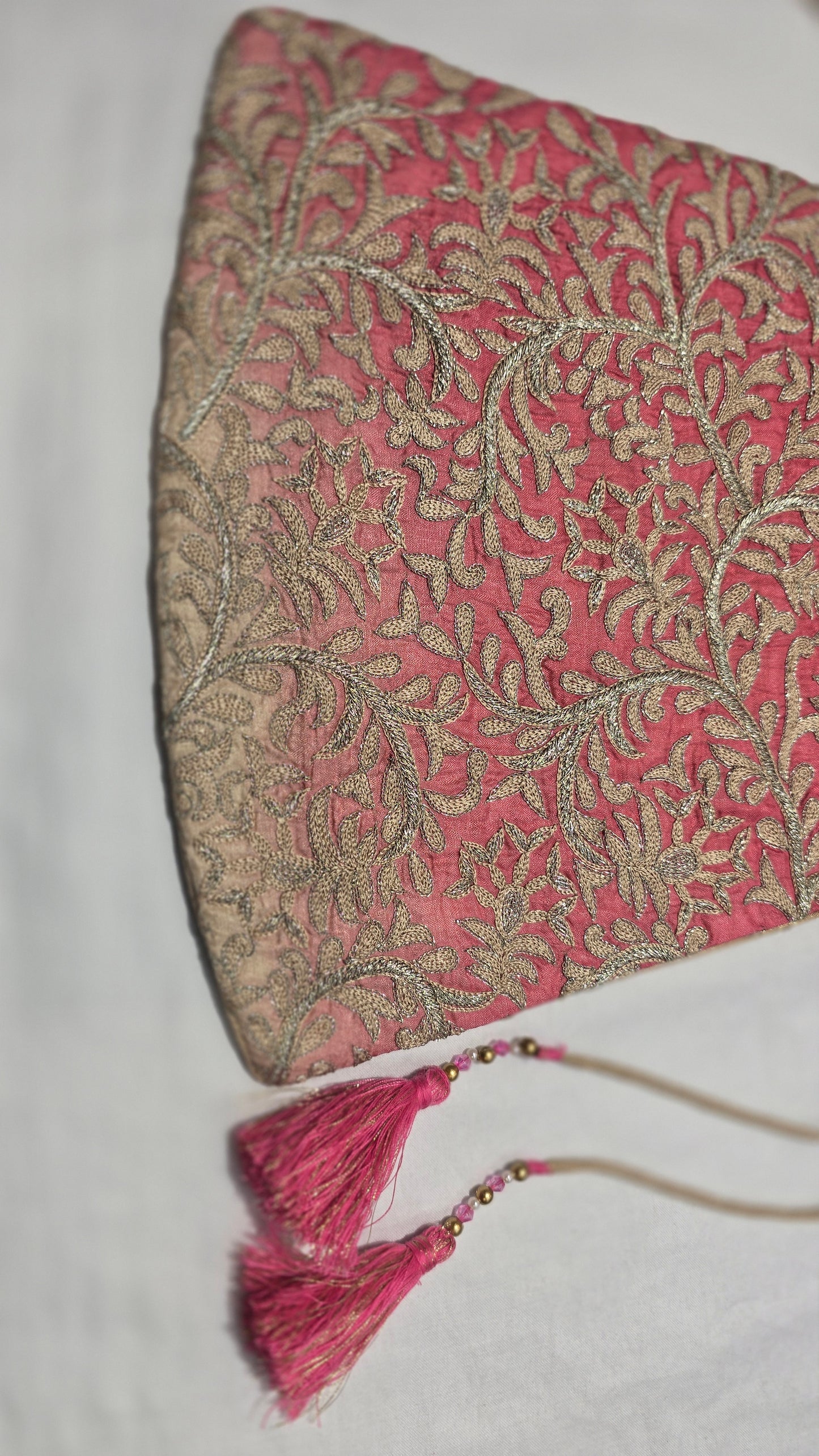 Decorative pink and gold handbag pouch with tassels on a white background